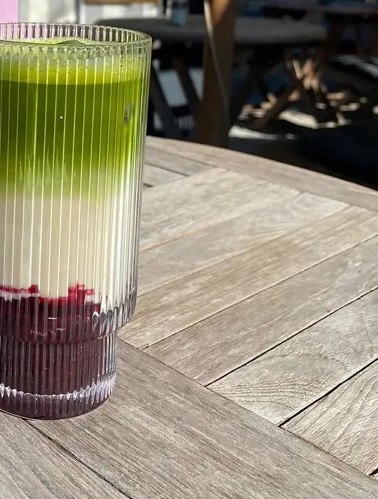 Iced Matcha Latte im geriffelten Glas auf dem Holztisch der Terrasse.