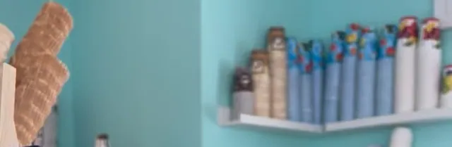Waffelhörnchen und Becher auf weißen Regalen vor der mintgrünen Wand im Laden.